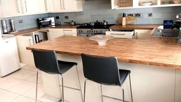 A modern kitchen with a wooden island, two black bar stools, a stainless steel stove, and white cabinets. - Spacious 3BR Home in Bedford for Big Groups (Bedford)