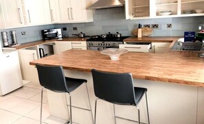 A modern kitchen with a wooden island, two black bar stools, a stainless steel stove, and white cabinets.
