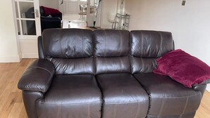 A dark brown leather sofa with a red throw pillow in a room with wooden flooring and a white door in the background. - Spacious 3BR Home in Bedford for Big Groups (Bedford)