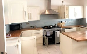 A compact kitchen with white cabinets, a stainless steel range hood, a built-in oven, and a microwave.