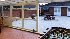 A covered patio area with a foosball table, brick walls, and a brick building in the background. - Spacious 3BR Home in Bedford for Big Groups (Bedford)