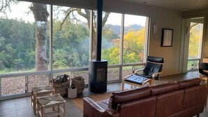 A cozy living room with a large window, a fireplace, a leather sofa, and a dining area with wicker chairs. - VIEWS!!  Last Minute/Longer Stay SPECIALS! (Ukiah Valley)