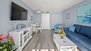 A living room with a blue sofa, white entertainment unit, and a flat-screen TV mounted on the wall. - Bay Watch 1706-1BR/1BA Oceanfront Condo in North Myrtle Beach (North Myrtle Beach)
