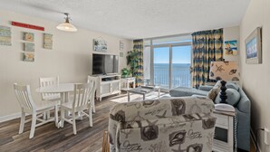 A living room with a dining area, a TV, and a balcony with curtains. - Bay Watch 1720-1BR/1BA Oceanfront Condo in North Myrtle Beach (North Myrtle Beach)