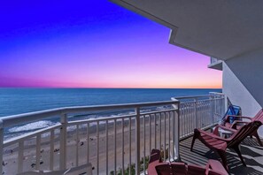 A balcony with a view of the beach and ocean during sunset.