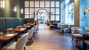 Ein Restaurant mit Holztischen und -stühlen, einer grünen Wand mit Leuchten und Blick durch große Fenster.