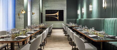 A restaurant with long tables, chairs, and a green upholstered booth.
