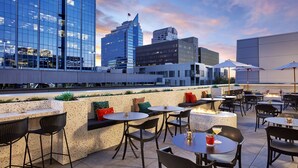 An outdoor seating area with tables and chairs, a fire feature, and a cityscape view in the background. - Hyatt Centric Downtown Sacramento (Sacramento)