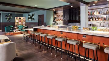 Zona de bar con varios taburetes, una barra con botellas y un área de estar con sillas y una mesa.