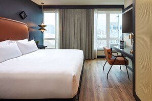 Une chambre d’hôtel avec un grand lit, un bureau et une vue sur la ville grâce à de grandes fenêtres.