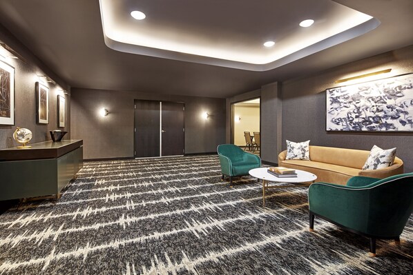 Un área de estar moderna con alfombra estampada, un sofá, sillones, una mesa de centro y un escritorio con lámpara.