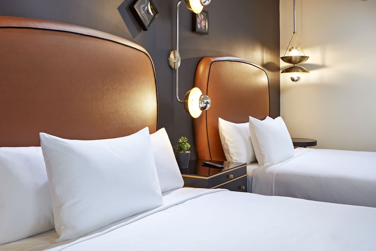 A hotel room with two beds, a nightstand, a mirror, and wall-mounted lighting.