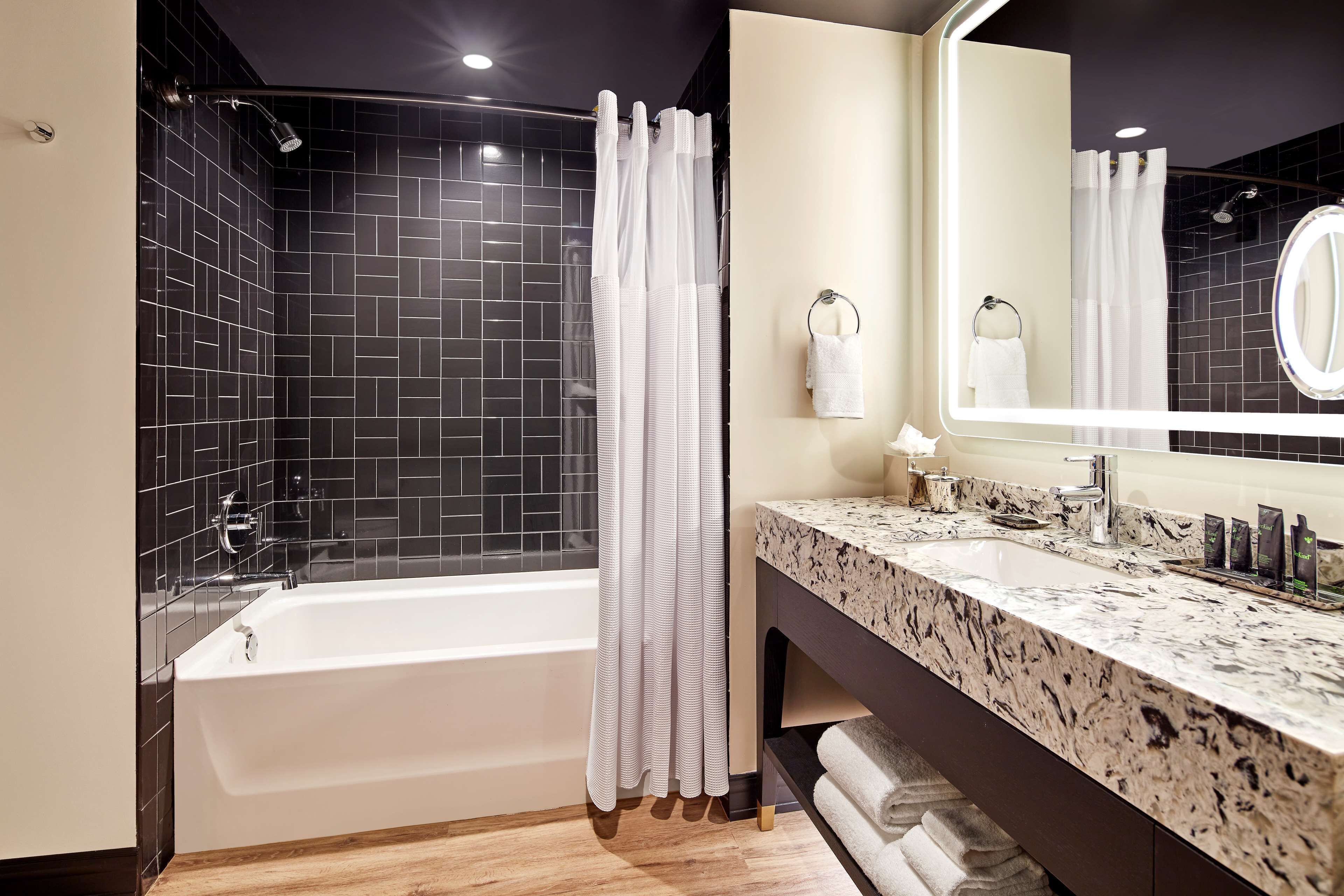 A modern bathroom with a black tiled shower, a white bathtub, a marble sink, and a large mirror.
