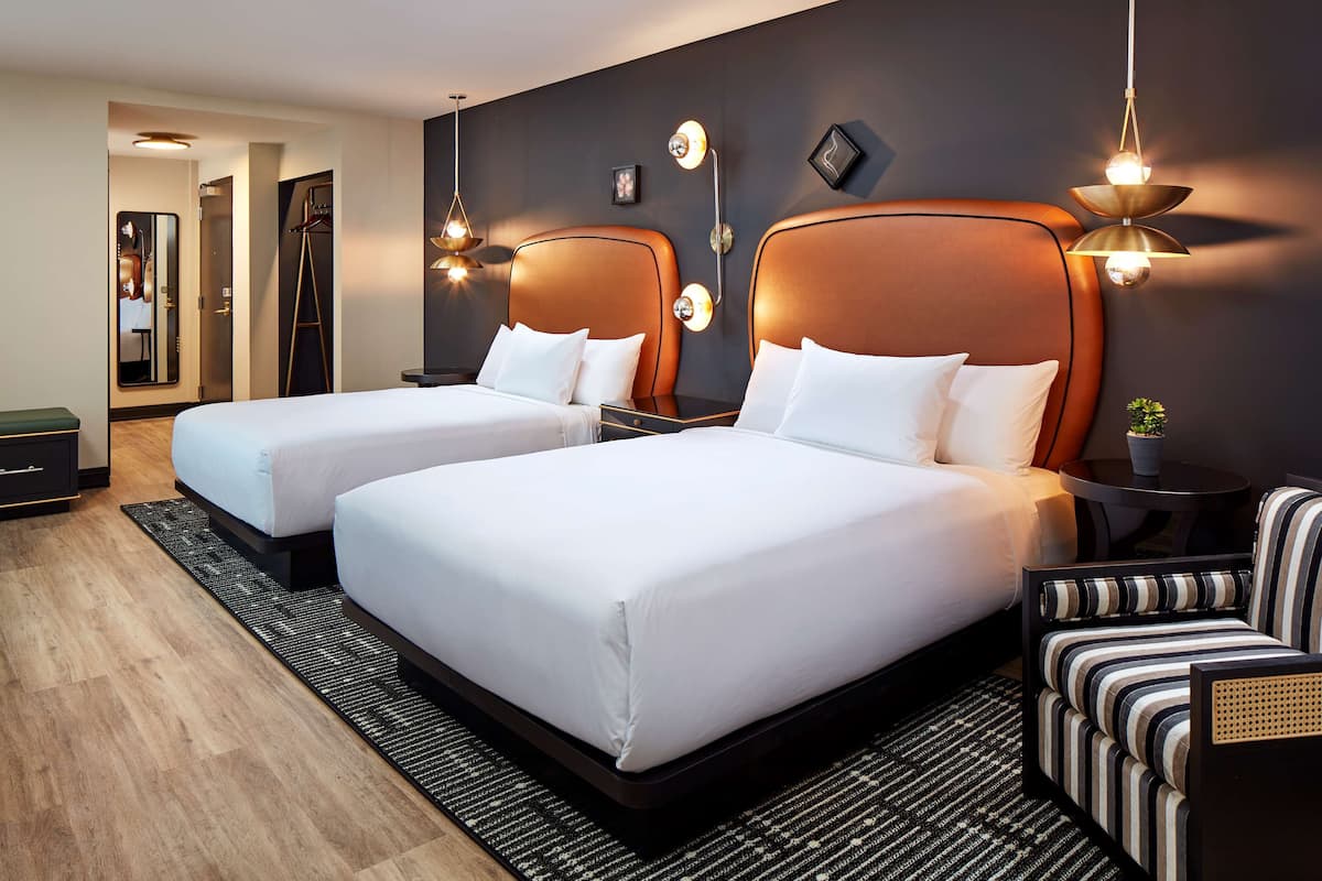 A hotel room with two beds, a small table, a chair, and a mirror.