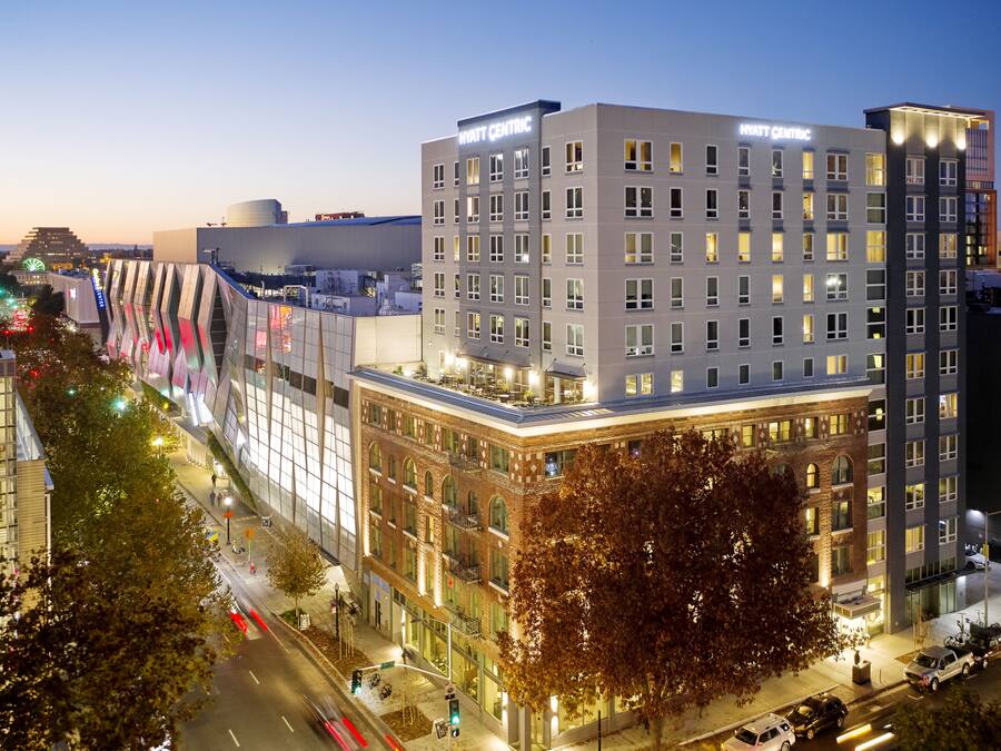 A modern hotel with a prominent 'Hyatt Centric' sign, featuring a mix of traditional and contemporary architecture, located in an urban setting with visible street and traffic.
