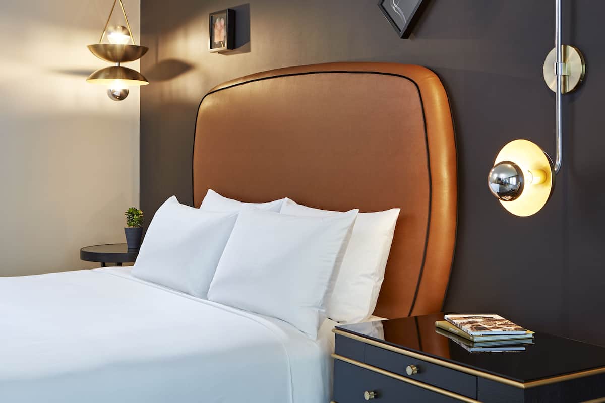 A neatly made bed with white linens, a dark headboard, and a bedside table with a lamp and a book.