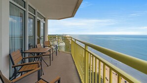 Ein Balkon mit Tischen und Stühlen mit Blick auf einen Strand und den Ozean.