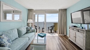 A living room with a sofa, a coffee table, a television, and a balcony with a view.
