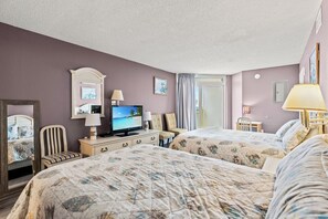 Ein Hotelzimmer mit zwei Betten, einem Fernseher, einem Schreibtisch mit Lampe und einem Sessel.