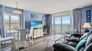 Un salon comprenant un coin repas, une grande fenêtre offrant une belle vue et une décoration murale sur le thème de la plage.