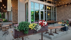 An outdoor seating area with tables and chairs, a neon sign, and flower arrangements. - TownePlace Suites by Marriott Rochester Mayo Clinic Area (Rochester)