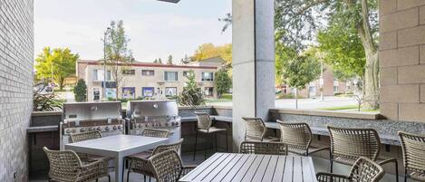 An outdoor patio with a grill, tables, and wicker chairs.