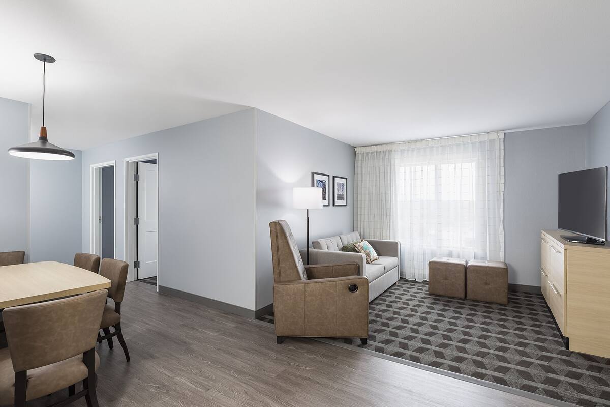 Ein modernes Hotelzimmer mit Essbereich, einer Couch, einem Fernseher und einem gemusterten Teppich.