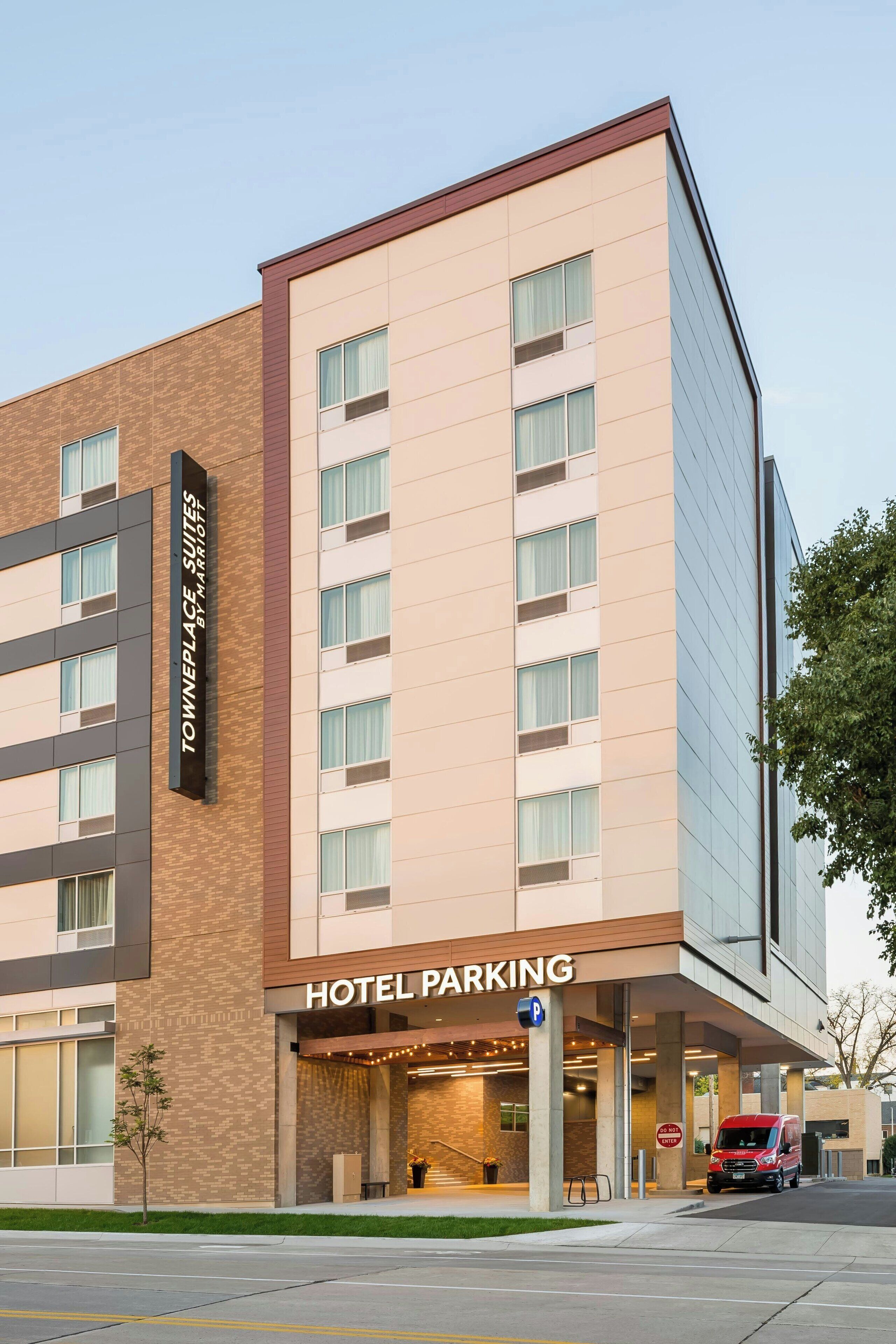 Entrada de un estacionamiento de hotel, con un letrero que dice "TownePlace Suites by Marriott" y una camioneta roja visible.