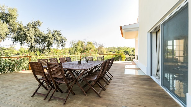 Une terrasse en bois avec une table et des chaises, donnant sur un jardin arboré et délimité par une clôture.