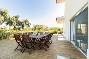 Une terrasse en bois avec une table et des chaises, donnant sur un jardin arboré et délimité par une clôture.