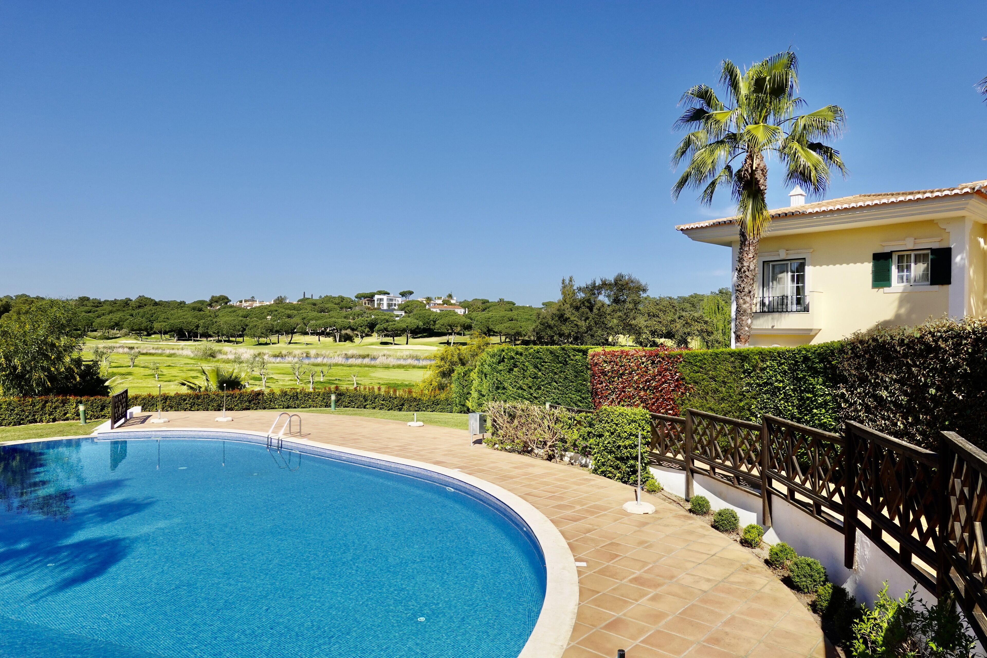 Une piscine à bordures courbes, entourée d’une terrasse carrelée et d’une clôture en bois.