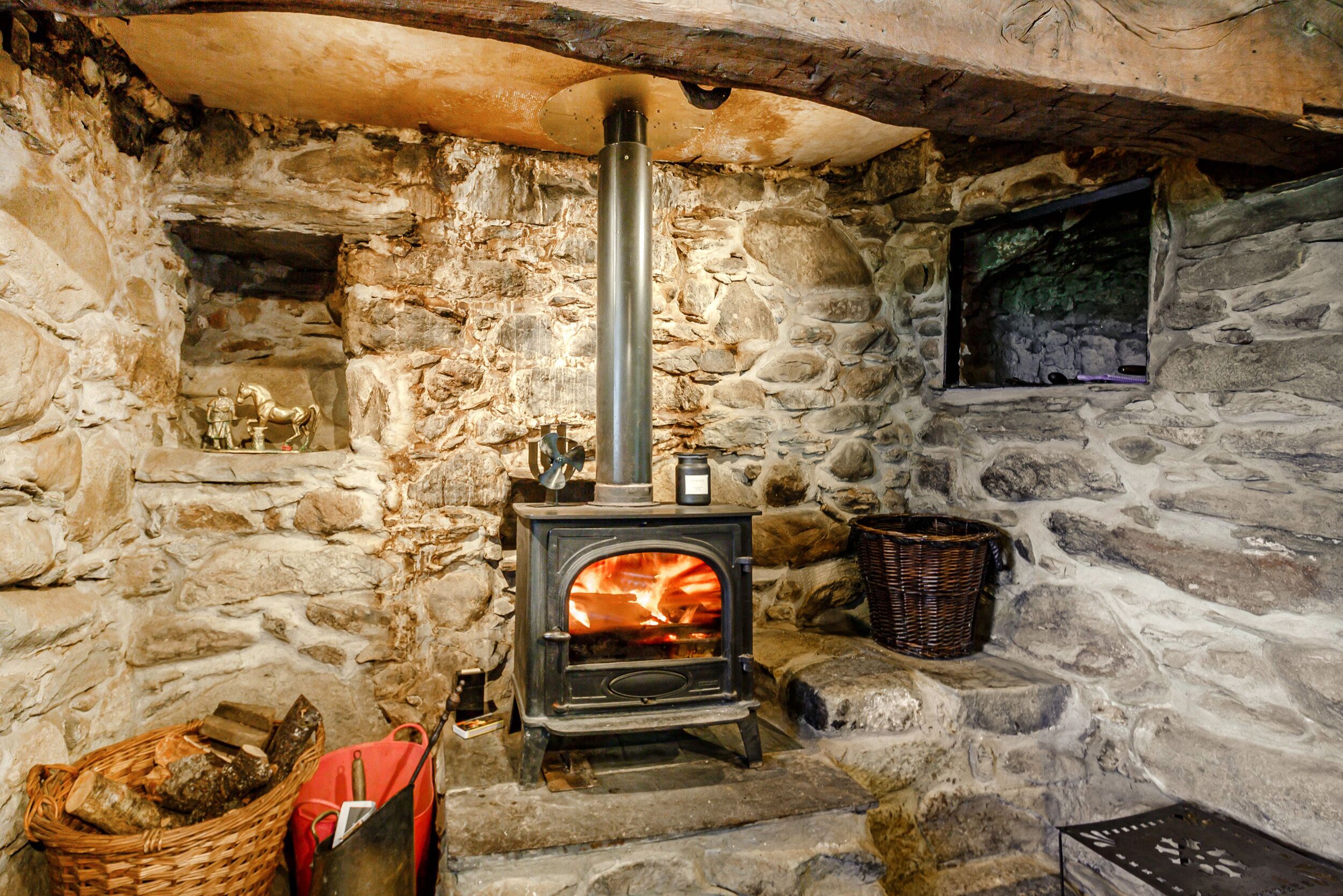 A stone-walled room with a wood-burning stove, a basket, and a basket of firewood.