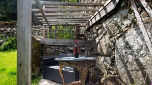 Eine Steinsäule, eine Holzpergola und ein runder Tisch mit zwei Weingläsern und einer Weinflasche.