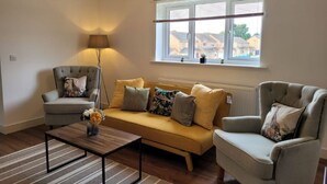 A living room with a sofa, two armchairs, a coffee table, and a lamp. There is a window with blinds and a view of houses outside.