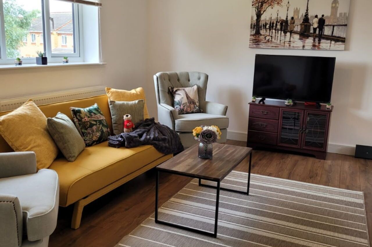 A living room with a sofa, armchair, coffee table, TV, and a cabinet.