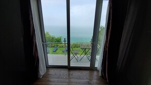 A room with a wooden floor, a sliding glass door leading to a balcony with a view of the sea. - Sunset and Serenity (Benton Harbor)