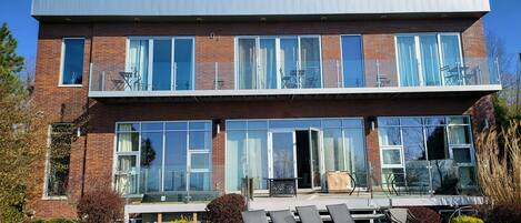 A modern two-story house with large windows, a balcony, and outdoor seating.