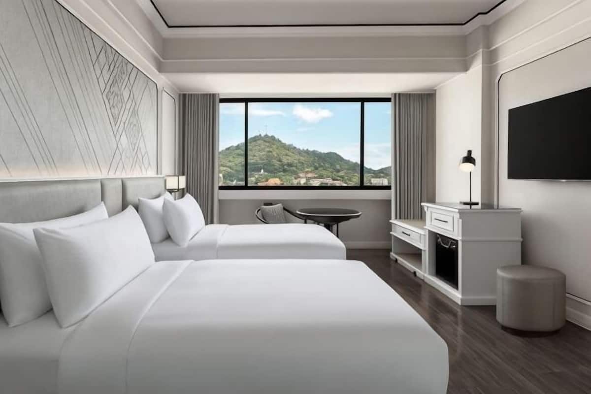 Habitació d'hotel amb dos llits, una taula, una cadira, un televisor i vista a una muntanya.