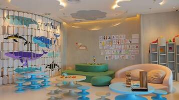 Une salle de jeux pour enfants avec une fresque murale, plusieurs coins salon et des éléments de décoration murale à vocation éducative.
