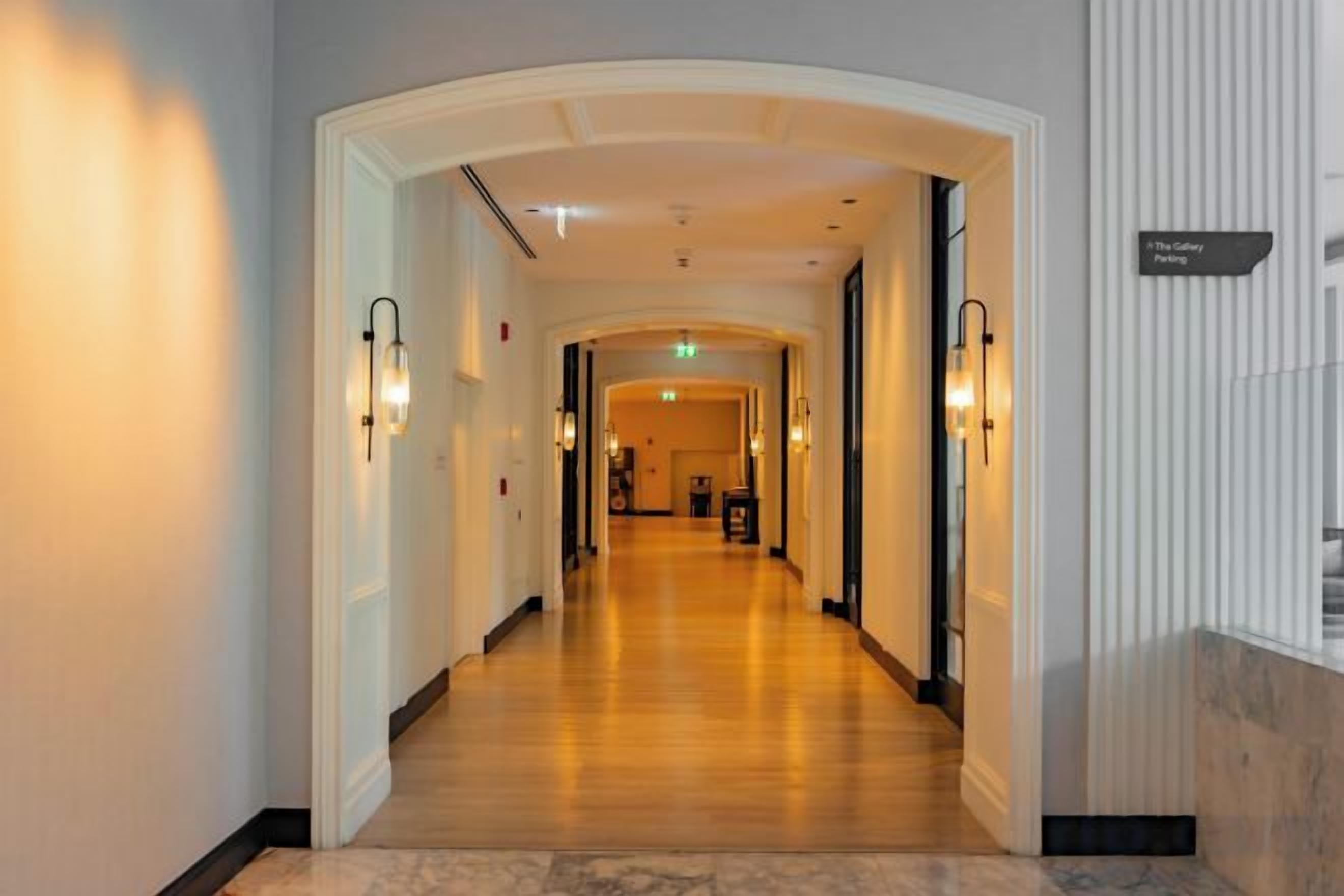 A hotel corridor with a wooden floor, white walls, and a sign indicating the direction to the lobby.