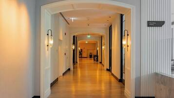 A hotel corridor with a wooden floor, white walls, and a sign indicating the direction to the lobby.