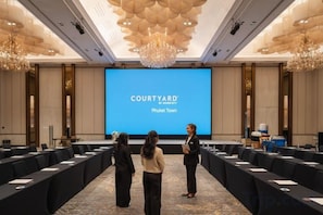 A conference room with a large screen displaying 'COURTYARD by Marriott Phuket Town,' a long table with chairs, and a chandelier. - Courtyard by Marriott Phuket Town (Phuket)