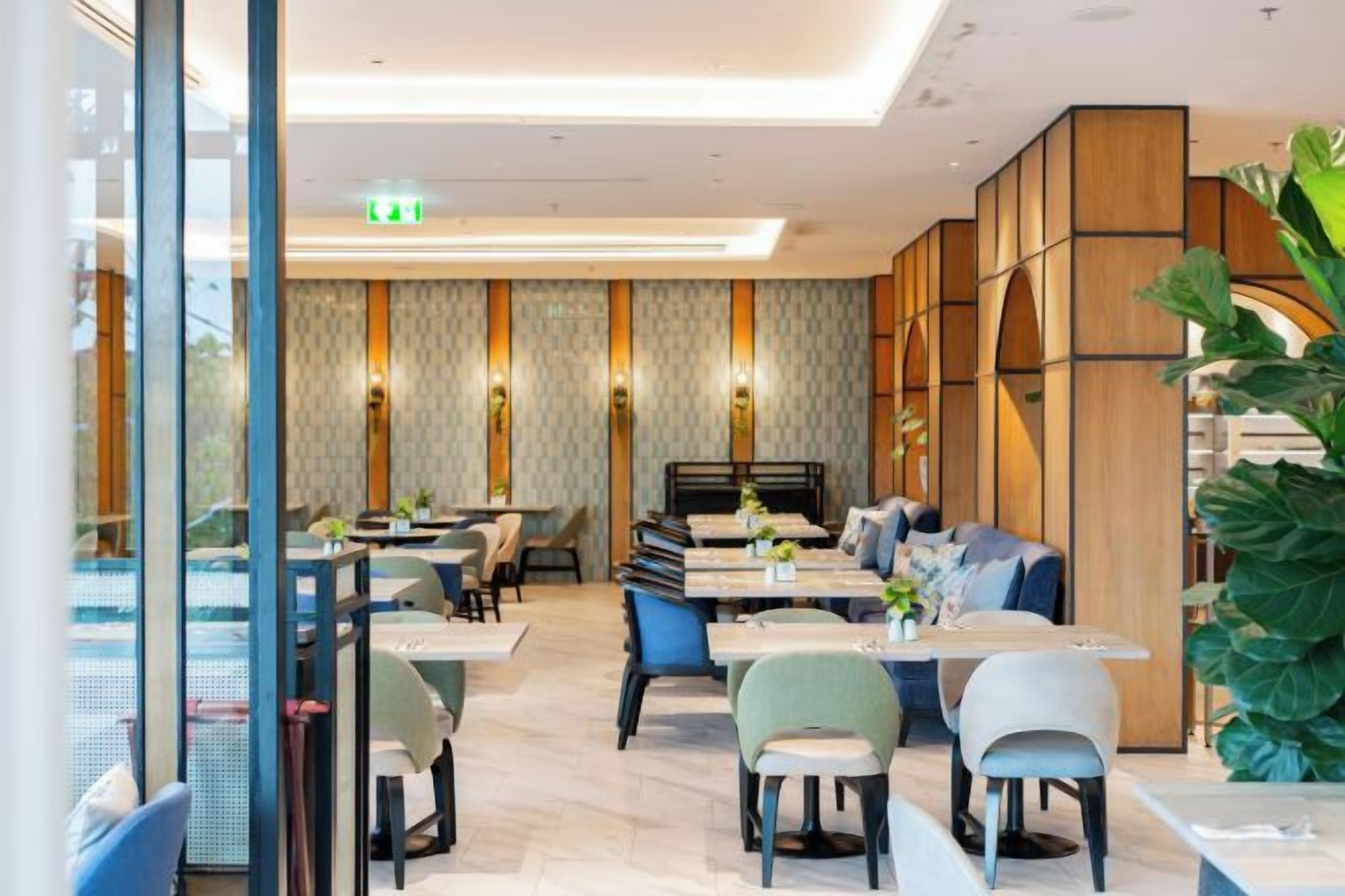 Un espace de repas moderne avec des tables et des chaises, un canapé et une grande plante.