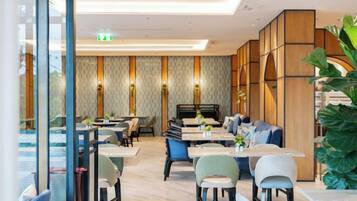 Un espace de repas moderne avec des tables et des chaises, un canapé et une grande plante.