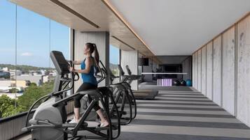 Une salle de sport équipée de tapis de course et d’appareils d’exercice, dotée de grandes fenêtres et offrant une vue sur la ville.