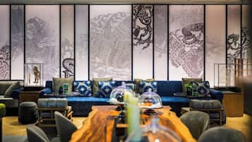 A modern interior with a wooden dining table, blue sofa with patterned cushions, and traditional artwork on the wall.