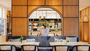 Un restaurant doté d’un espace de restauration central, d’une grande plante et d’une vue sur la cuisine.