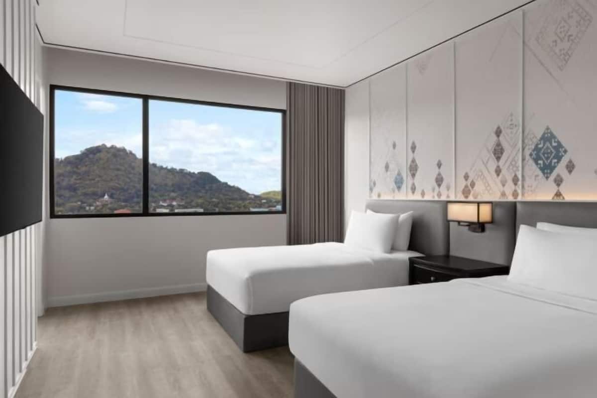 Habitació d'hotel amb dos llits, una finestra gran amb vista a les muntanyes, un televisor de pantalla plana i una làmpada penjada a la paret.