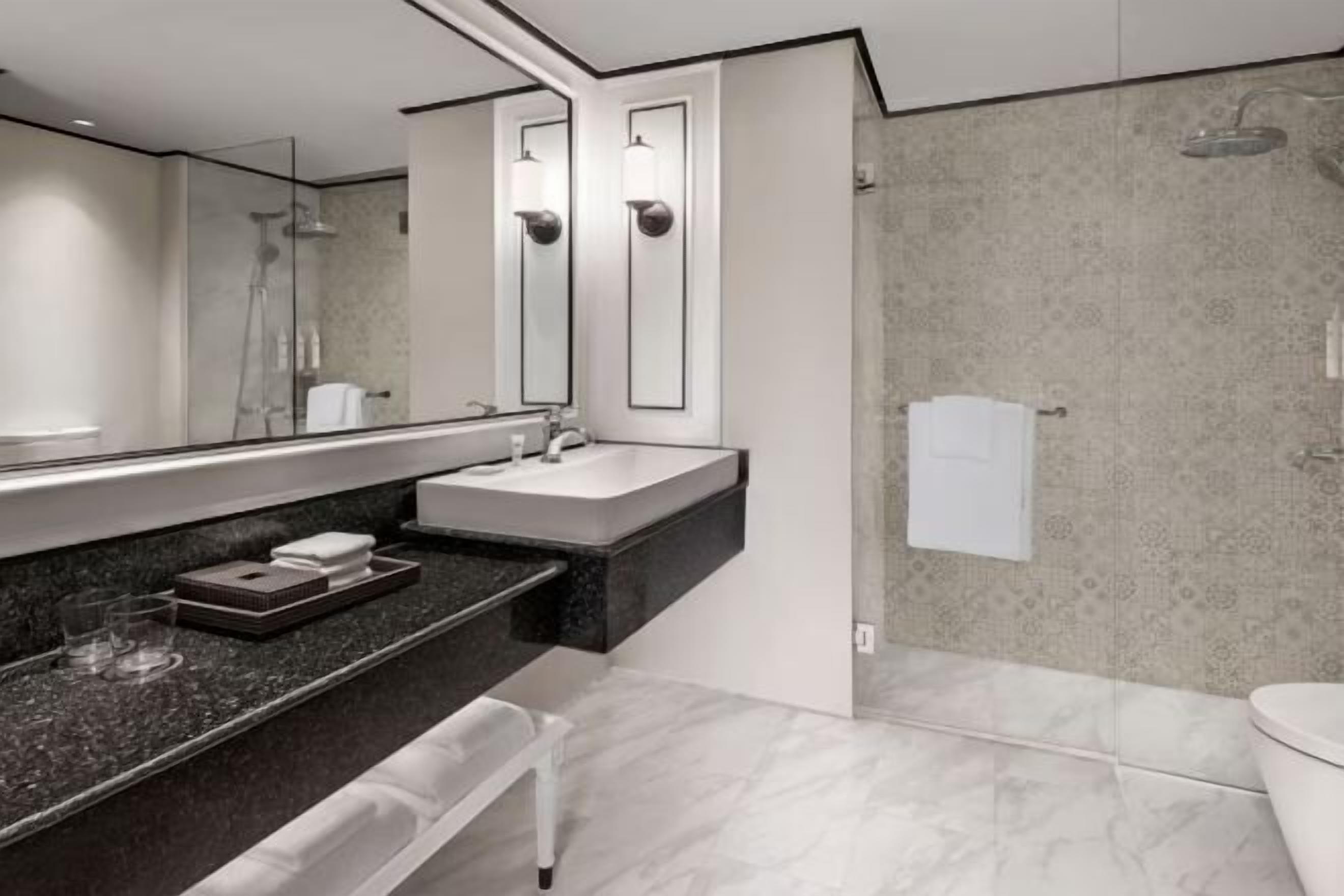 A modern bathroom with a large mirror, a sink, a shower, and a toilet.