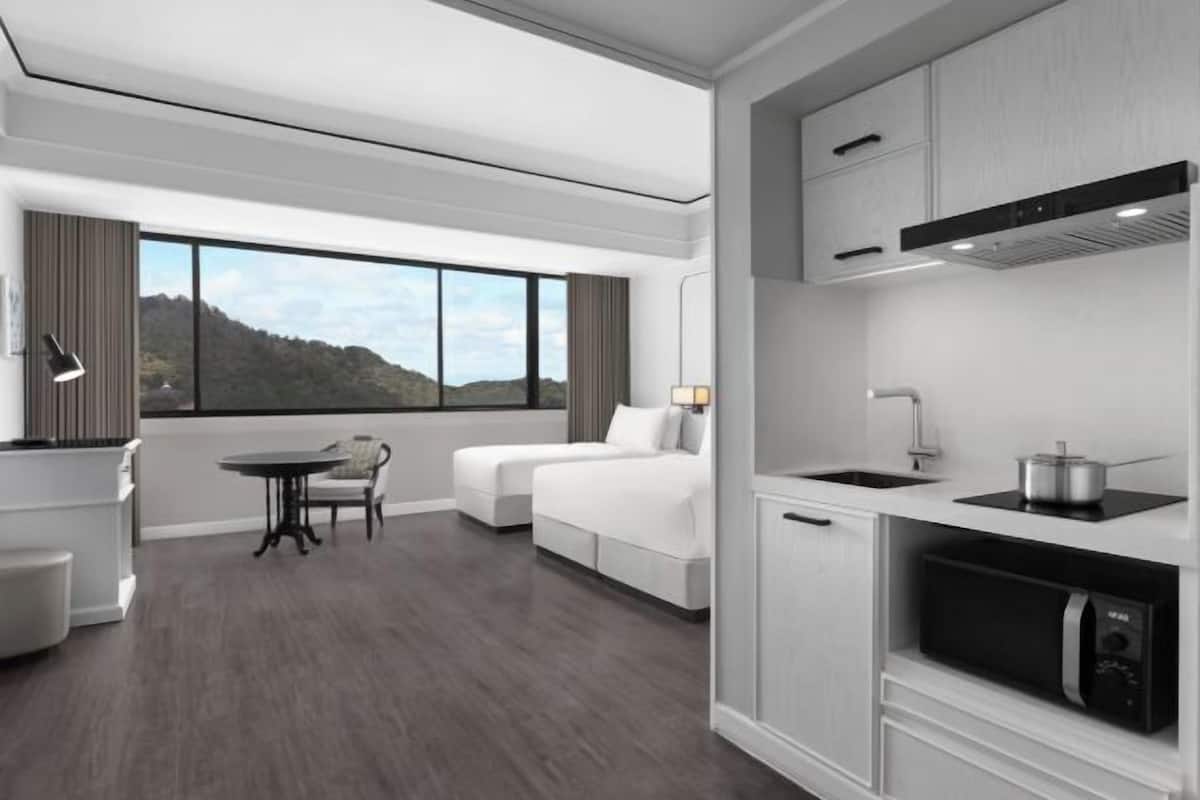 Habitació d'hotel moderna amb una finestra gran, zona de menjador, petita cuina i un llit.